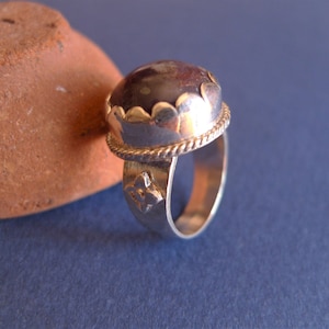 Può includere: Un anello d'argento con una pietra grigio scuro incastonata in una montatura d'argento. L'anello ha una fascia decorativa con motivi floreali.