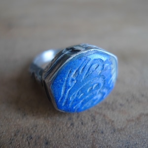 Pu&ograve; includere: Un anello d'argento con una pietra di lapislazzuli blu incastonata in una forma esagonale. La pietra &egrave; scolpita con un disegno.