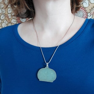May include: A silver chain necklace with a light green pendant shaped like a vase with a floral design.
