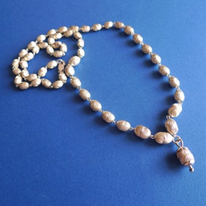 May include: A silver necklace with a pendant made of oval-shaped beads. The beads have a textured, wavy design. The necklace is on a blue background.