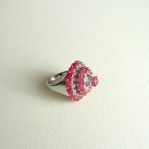 Può includere: Un anello d'argento con un grande gruppo di pietre preziose rosa a forma di cono. L'anello è incastonato con molte piccole pietre preziose rosa rotonde.