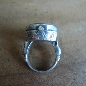 Pu&ograve; includere: Un anello d'argento con un designo ornato sulla parte superiore e una fascia liscia. L'anello &egrave; fatto di metallo e ha una forma circolare.