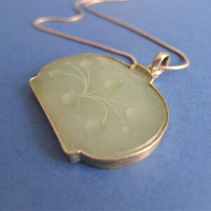 May include: A silver chain necklace with a green jade pendant featuring a floral design.