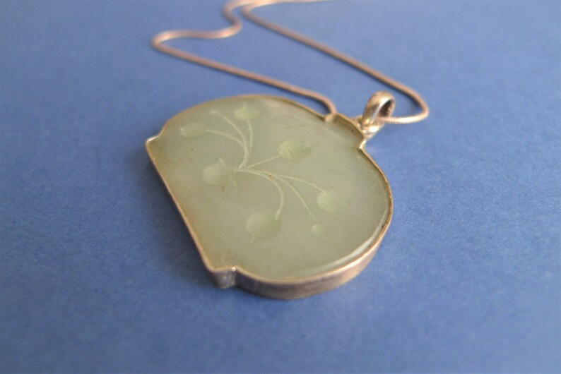 May include: A silver chain necklace with a green jade pendant featuring a floral design.