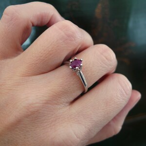 May include: A silver ring with a red ruby gemstone set in a crown-shaped setting.