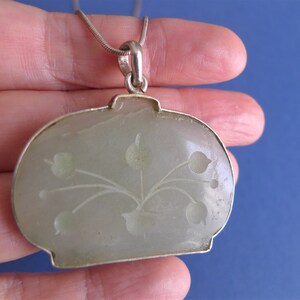 May include: A silver chain necklace with a jade pendant. The pendant is carved with a floral design.