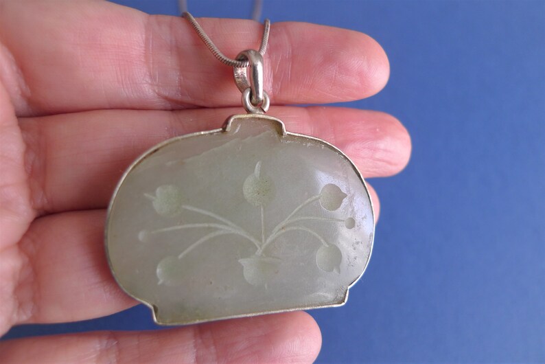 May include: A silver chain necklace with a jade pendant. The pendant is carved with a floral design.