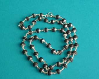 May include: A necklace with dark, round beads strung on silver-colored wire. The beads are evenly spaced and the wire is intricately wrapped between them. The necklace is displayed against a teal background.