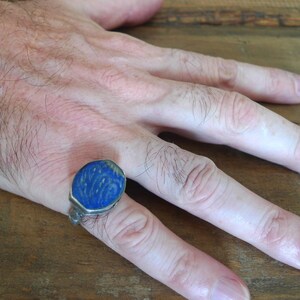 Pu&ograve; includere: Un anello d'argento con una pietra di lapislazzuli blu incastonata in una montatura a castone. La pietra &egrave; scolpita con disegni intricati.