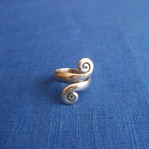 May include: A silver ring with two spiral designs. The ring is on a blue fabric background.