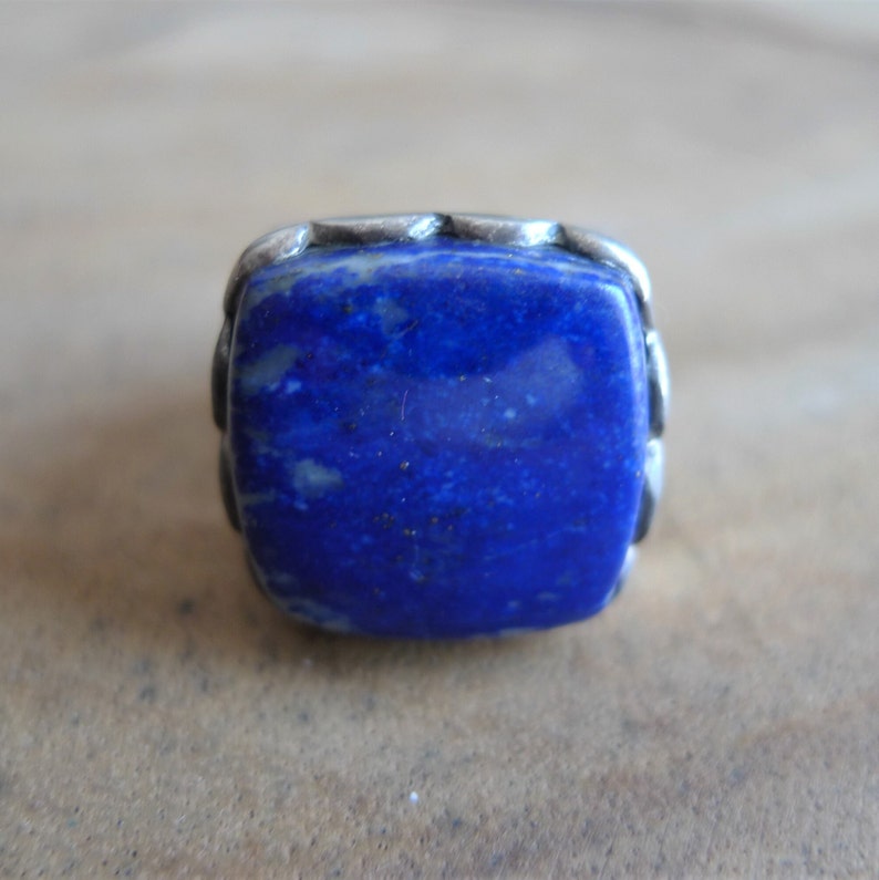 May include: A square-shaped ring with a deep blue lapis lazuli stone set in a silver band.
