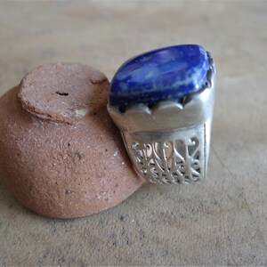 May include: A silver ring with a large, square, blue lapis lazuli stone set in the center. The ring band is intricately designed with a filigree pattern.