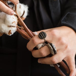 Könnte beinhalten: Eine Hand trägt einen silbernen Ring mit einem schwarzen geometrischen Design. Der Ring befindet sich am Zeigefinger und es befindet sich ein zweiter Ring am Mittelfinger.