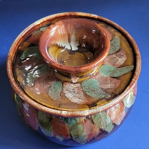 May include: A brown ceramic serving dish with a lid and a small bowl in the center. The dish and lid are decorated with a brown, green, and white abstract pattern.