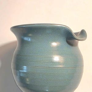 May include: A handcrafted, blue-green ceramic vase with a unique, ruffled rim. The vase has a rounded body and a textured surface, showcasing the artisan's touch. This decorative piece is ideal for displaying flowers or as a standalone art object.