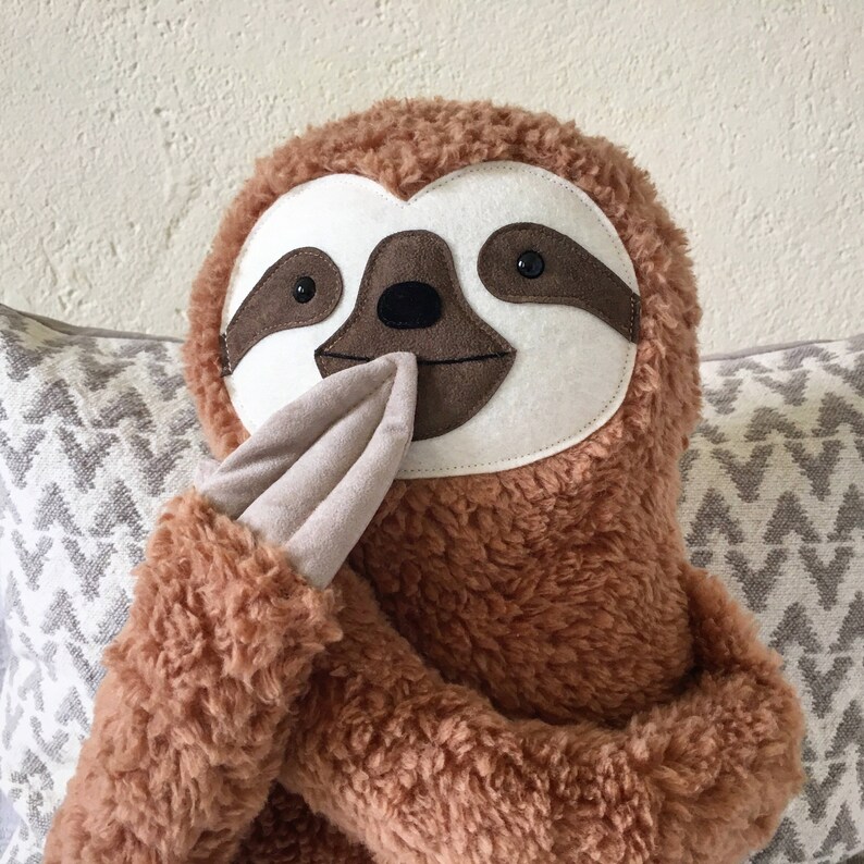 May include: A brown plush sloth toy with a white face and black eyes. The sloth is holding its hands in front of its face.