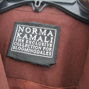 Pu&ograve; includere: Una camicia marrone con un'etichetta nera che recita "Norma Kamali The Exclusive Collection for Bloomingdales".