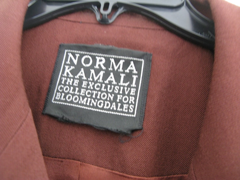 Pu&ograve; includere: Una camicia marrone con un'etichetta nera che recita "Norma Kamali The Exclusive Collection for Bloomingdales".
