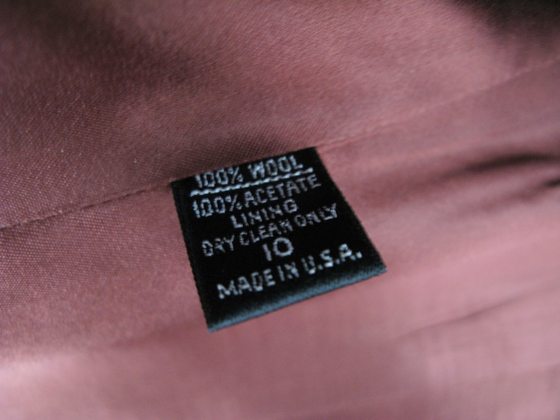 Pu&ograve; includere: Un'etichetta in tessuto nero con testo bianco che recita "100% Lana 100% Acetato Fodera Lavaggio a secco solo 10 Made in USA."