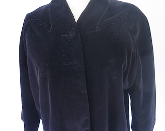 Puede incluir: Una chaqueta de terciopelo azul marino oscuro con un cuello chal ancho, mangas tres cuartos y un cierre de un solo botón grande cubierto de tela en la parte delantera. La prenda presenta costuras curvas en el área del pecho.