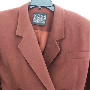Pu&ograve; includere: Un blazer marrone con chiusura a un solo bottone e una tasca sul lato destro. L'etichetta recita "Norma Kamali The Exclusive Collection for Bloomingdales".