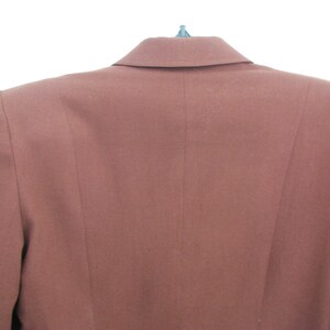 Pu&ograve; includere: Un blazer marrone con una chiusura a un solo bottone e un colletto a punta.