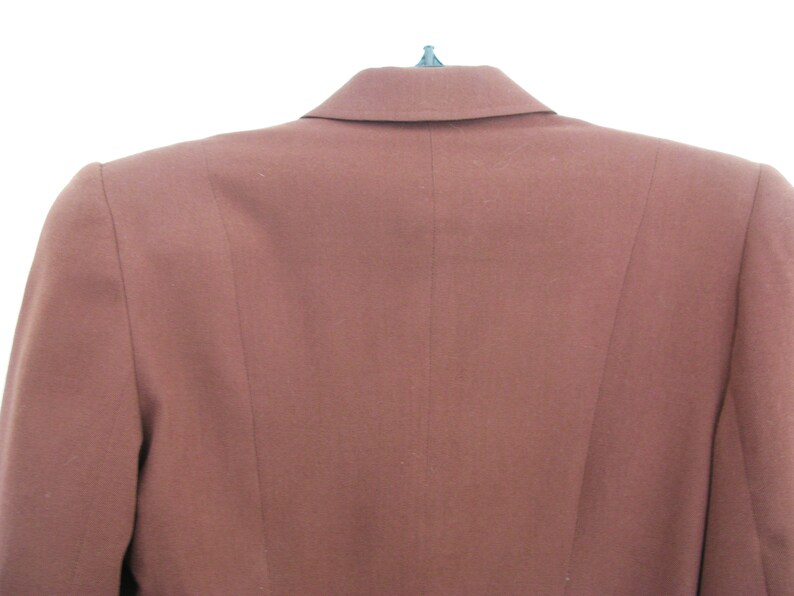 Pu&ograve; includere: Un blazer marrone con una chiusura a un solo bottone e un colletto a punta.