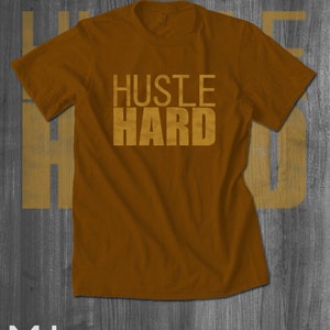 May include: A brown t-shirt with the words "Hustle Hard" printed in gold on the front.