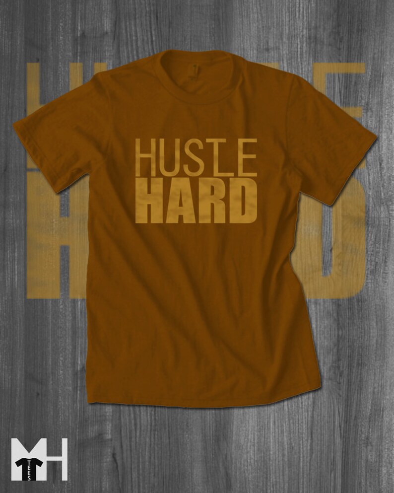 May include: A brown t-shirt with the words "Hustle Hard" printed in gold on the front.