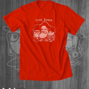 May include: Red t-shirt with a white graphic of three cartoon beans wearing hats and sunglasses. The text "Cool Beans" is printed above the beans.