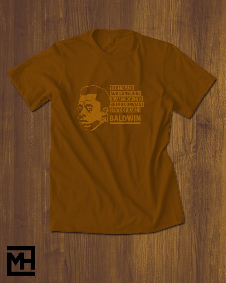 May include: A brown t-shirt with a black and white illustration of James Baldwin. The text on the shirt reads "To be black and conscious in America is to be in a constant state of rage! Baldwin."