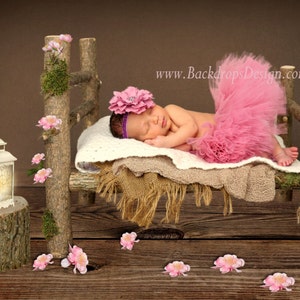 May include: A newborn baby girl wearing a pink tutu and a flower headband sleeps on a rustic wooden bed with a white blanket and a brown blanket. The bed is decorated with pink flowers and a lantern.