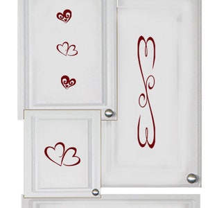 Puede incluir: Puertas de armario blancas con un cajón, con un diseño de corazón rojo. Las puertas y el cajón tienen detalles decorativos y pomos plateados.