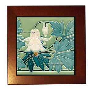 May include: A vintage ceramic tile with a green background featuring a white flower with blue-green leaves. The tile is framed in a dark wood frame.