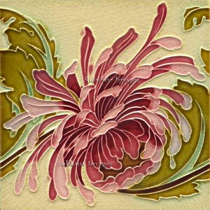 May include: A vintage ceramic tile featuring a stylised floral design. The tile depicts a pink and red chrysanthemum flower with green leaves on a cream background.