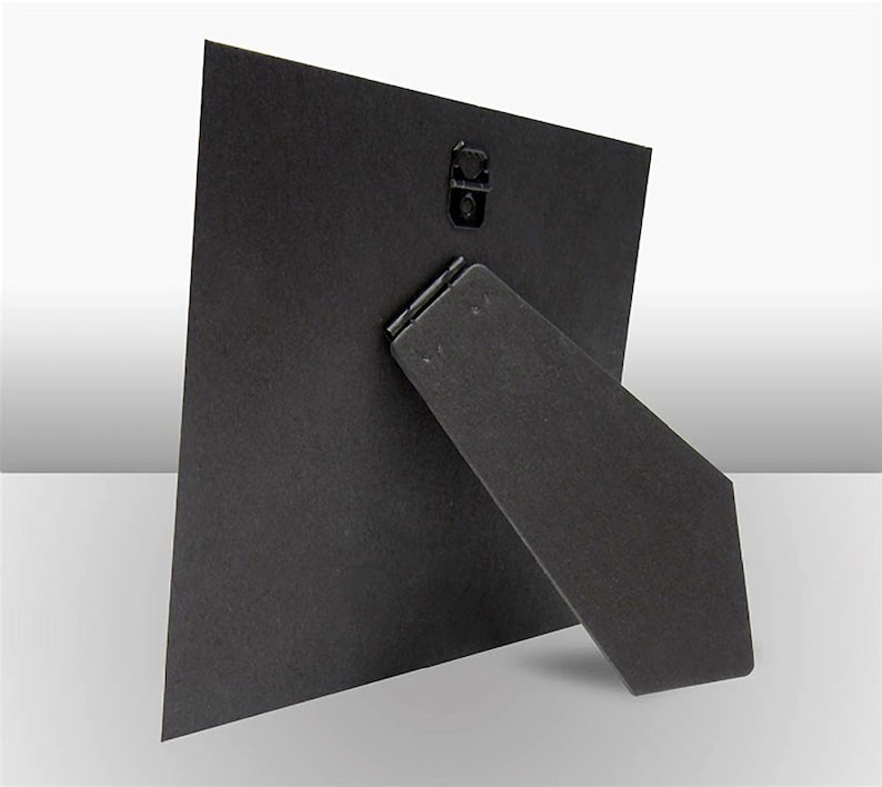 May include: Black cardboard photo frame with a built-in easel stand on the back. The frame is designed to stand upright on a table or shelf.