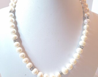 May include: A cream-colored pearl necklace with silver accents. The necklace is composed of round pearls, interspersed with small silver sections. The necklace is displayed on a white mannequin bust.
