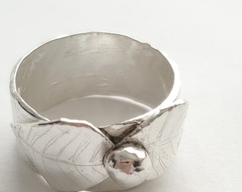 May include: A silver ring with a leaf and berry design. The ring features two detailed leaves on either side of a small, round berry. The ring is made of a shiny, silver metal.