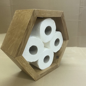 May include: A hexagonal wooden toilet roll holder with four rolls of toilet paper inside. The holder is made of light brown wood and has a rustic look.