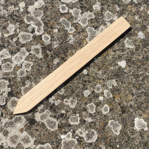 May include: A wooden plant marker with a pointed end. The marker is light brown and has a smooth surface.