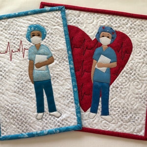 May include: Two quilted wall hangings featuring a stylized image of a healthcare worker wearing a surgical cap, mask, and scrubs. The left image has a red EKG line and the right image has a red heart with an EKG line.