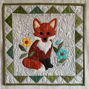 May include: A square fabric wall hanging featuring a central applique of a rust-colored fox with white chest fur and black paws. The fox is surrounded by a yellow flower and a blue flower on a white background with swirling quilted patterns.