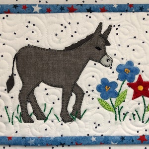 May include: A grey donkey with a white face stands in a field of green grass and blue and red flowers. The donkey is looking to the right. The background is white with a blue and red border.