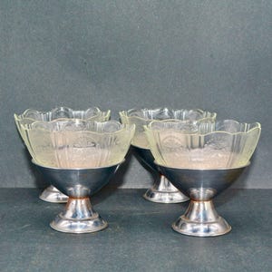 May include: Four vintage dessert bowls with clear, scalloped glass tops and silver-colored metal bases. The bowls are arranged in a group, showcasing their elegant design. The background is a solid, dark gray.