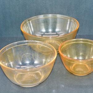 Peut inclure: Trois bols en verre transparents avec une teinte orangée. Les bols sont emboîtés, avec un grand, un moyen et un petit. Les bols ont une forme arrondie et sont en matériau transparent.
