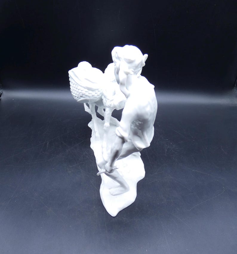 Może przedstawiać: Biała porcelanowa figurka przedstawiająca osobę trzymającą koszyk z dzieckiem w środku. Figurka stoi na podstawie z fakturowaną powierzchnią.