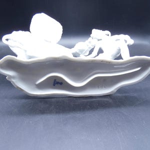 Może przedstawiać: Biała porcelanowa figurka kobiety jeżdżącej konno. Figurka stoi na białej podstawie z niebieskim znakiem, na kt&oacute;rym widnieje napis "1882".