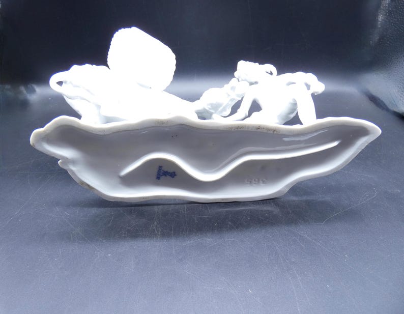 Może przedstawiać: Biała porcelanowa figurka kobiety jeżdżącej konno. Figurka stoi na białej podstawie z niebieskim znakiem, na kt&oacute;rym widnieje napis "1882".