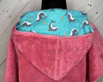 May include: A pink hooded towel with a teal lining patterned with grey narwhals and orange starfish. The towel is made of a soft, plush material, ideal for after bath or pool use.