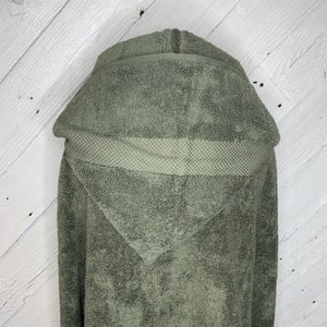 May include: A hooded towel in a muted green color. The towel is made of a soft, absorbent material and has a waffle-textured trim around the hood.